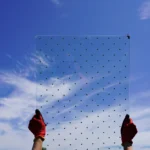 Glass treated with a bird-friendly pattern is held up with the sky as a background. Glass patterns are tested at ABC's testing tunnels.